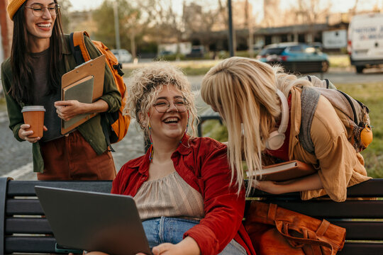 University friends laughing, studying together on campus bench