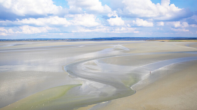 Person walking on vast tidal flat landscape in Mont Saint-Michel Bay, Normandy, France, Europe.
