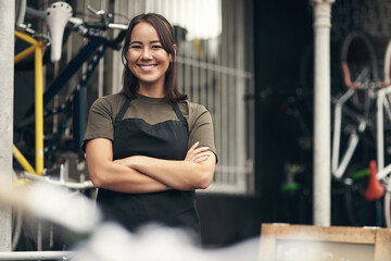Fototapeta premium Woman, happy and arms crossed at bicycle shop in portrait with pride, confidence and small business. Asian person, smile and mechanic for bike maintenance services, gear and job at garage in Cambodia