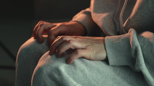 Man with trembling knees sitting on sofa in dark room. Concept of anxiety, fear, stress, nervous disorder, involuntary shaking, panic, and mental strain