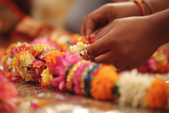 Creative composition of bride placing flower garland on groom during varmala ceremony with colorful flowers and decorations, warm lighting with copy space