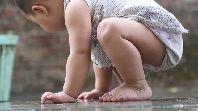 Adorable baby crouching and playing with rainwater on wet ground, capturing joyful childhood, curiosity, and carefree outdoor moment during monsoon.