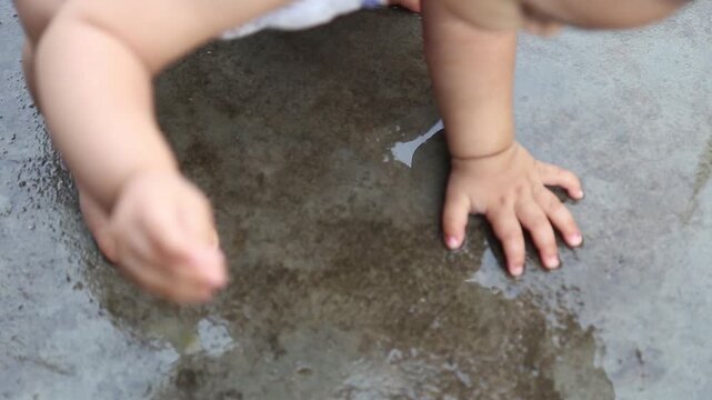 Adorable baby crouching and playing with rainwater on wet ground, capturing joyful childhood, curiosity, and carefree outdoor moment during monsoon.