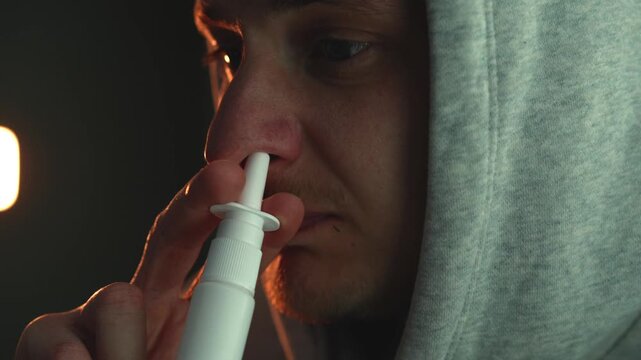 Close-up of a person treating blocked nose with nasal spray at night. Focus on respiratory health, allergy or cold symptoms, sinus relief, and medication use in a home environment