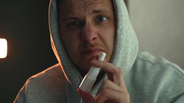 Person spraying nose to relieve nasal congestion in low light room. Concept of allergy relief, cold symptoms, sinus problems, breathing difficulty, and healthcare treatment at home.