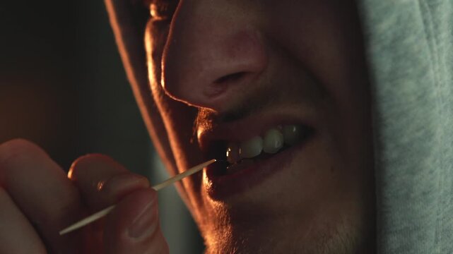 Young adult using a wooden toothpick after dinner in a cozy indoor setting. Concept of oral hygiene, dental care routine, removing food debris, healthy lifestyle and daily habits. Close-up, natural li