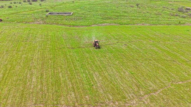 A tractor is working on a large open field, preparing the land for planting. The field is green, and a water source is visible in the background. This scene takes place in spring.
