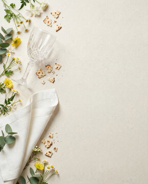 Spring floral arrangement, crystal wine glass, white linen napkin, matzo cracker crumb border