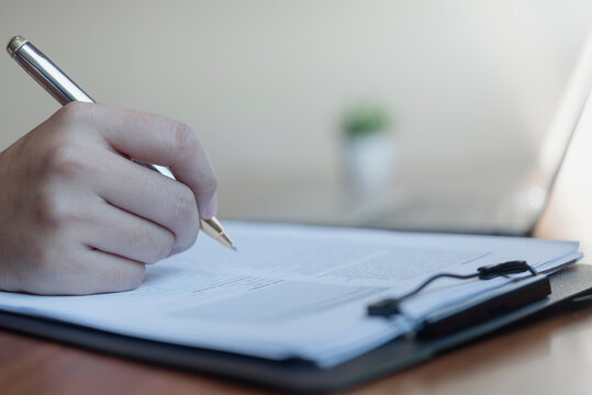 Business person hand holding pen signing legal contract document clipboard desk laptop corporate agreement official authorization B2B partnership paperwork compliance administration.