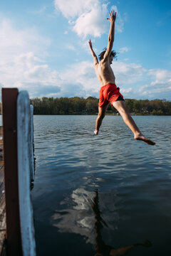 Teen boy jumping off dock into lake in summertime