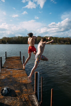 Big kids jumping into lake off dock on sunny afternoon
