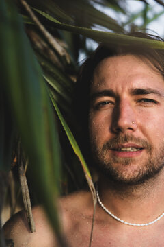 Young man with glitter face peeking through palm leaves, Bali