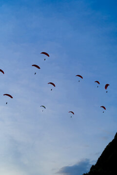 Many paragliders flying in blue sky over hills, Bali, Indonesia