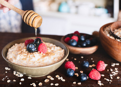 Berry oatmeal breakfast bowl ,drizzled honey in a rustic kitchen