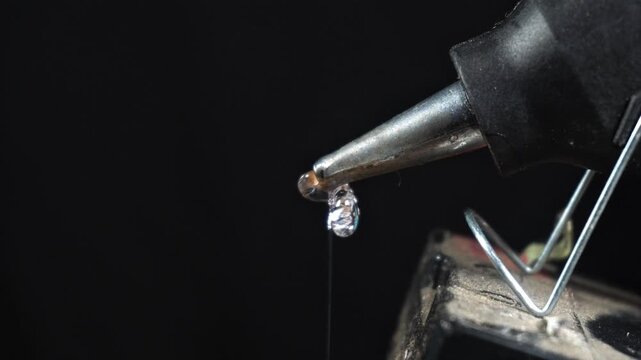 Hot Glue Gun Dripping Adhesive on Dark Background Macro Closeup. Hot Glue Dripping from Glue Gun Nozzle Closeup Dark Scene.