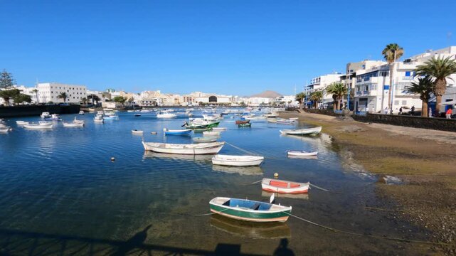 Tranquil lagoon of Charco de San Gin&eacute;s in Arrecife, Lanzarote, with colorful small fishing boats moored on calm blue water under clear sunny sky.