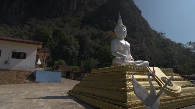 Tilt down reveal of golden lotus platform with pearl buddga sitting cross-legged in front of karst mountains.