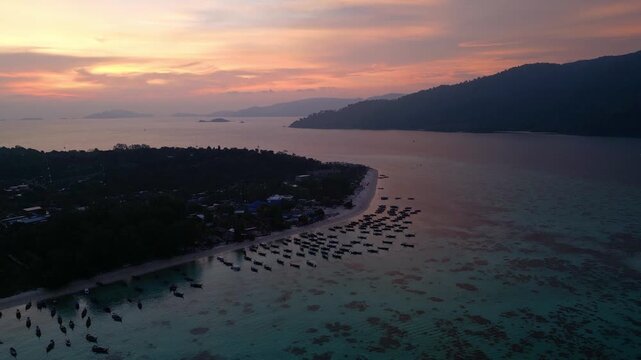 Koh Lipe, Thailand: Aerial drone footage of dramatic sunset over Koh Lipe, an island in Andaman sea of Thailand. Taken with forward and tilt up motion showing long tail boats by the beach
