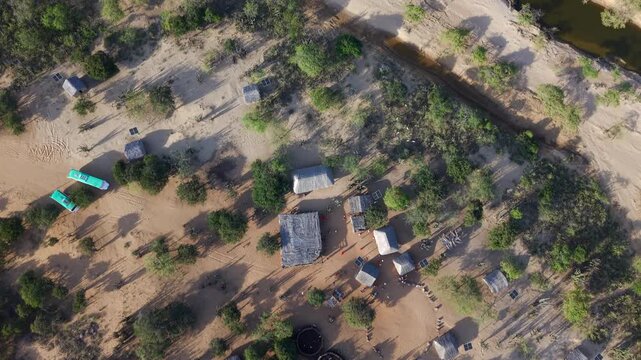 Drone footage captures the rustic beauty of a Wayuu village in La Guajira, Colombia. The sun casts long shadows across the vibrant landscape, revealing traditional homes among the desert scenery.