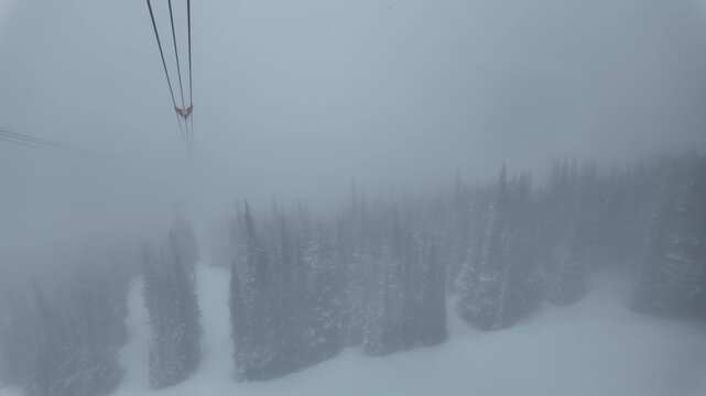 Heavy snowfall and dense fog over the pristine backcountry of Whistler. Aerial POV riding the PEAK 2 PEAK gondola connecting Whistler Blackcomb Mountain to Whistler Mountain Ski Resort.