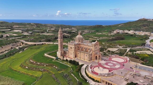 Santwarju Bażilika tal Madonna ta&rsquo; Pinu in Għarb Gozo Malta stands isolated within rural landscape featuring limestone baroque architecture and open fields, aerial drone orbit establishing shot