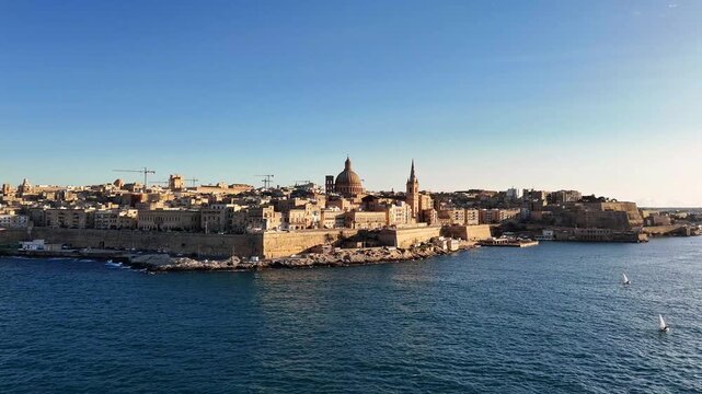 Basilica of Our Lady of Mount Carmel rises over Valletta Malta skyline with Grand Harbour fortifications, Floriana bastions and limestone buildings along Triq ir-Repubblika and waterfront, static shot