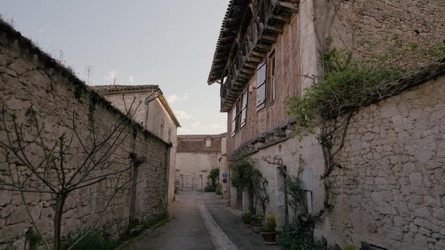 Stone buildings and traditional timber-framed architecture line a narrow medieval street in the bastide of Issigeac, Dordogne. Forward tracking shot.