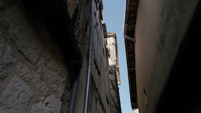 Upward view of a tight street in the bastide of Issigeac, showcasing traditional architecture and ancient stone walls. Low-angle shot.