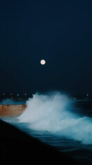 Fototapeta premium Full moon illuminating powerful ocean wave crashing against a concrete seawall during a dark night with distant city lights creating a serene coastal scene