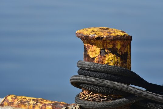 Black nylon double braided mooring ropes on a rusty yellow bollard against the blue sea.