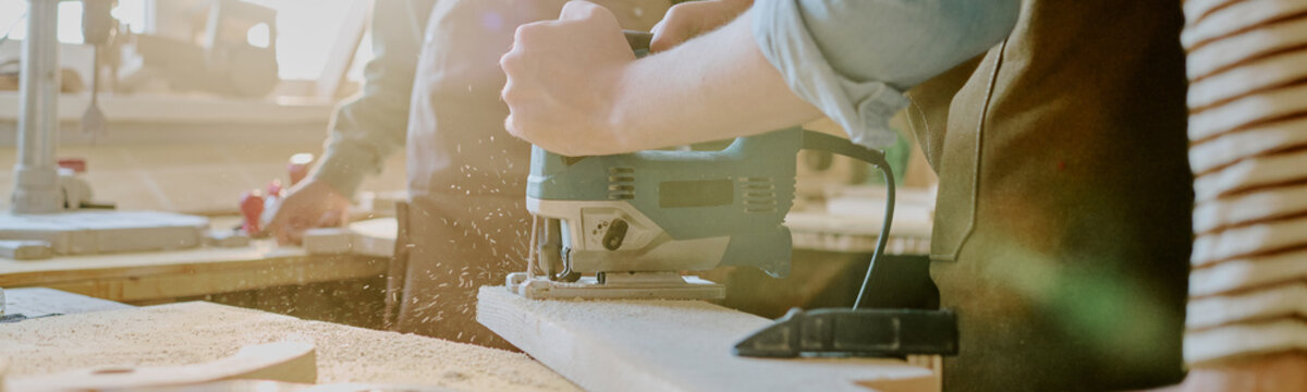 Header of carpenter cutting wood with electric jigsaw in workshop, creating sawdust during fabrication. Ideal for construction services, skilled trades, DIY marketing