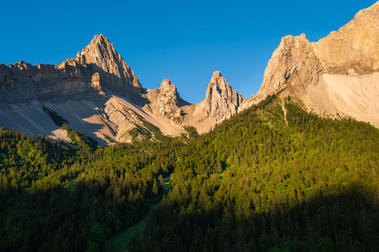 Aerial view of La Jarjatte in the Devoluy massif, Drome, France, with limestone peaks, and conifer forest. Alpine valley in the French Alps under warm summer sunset light