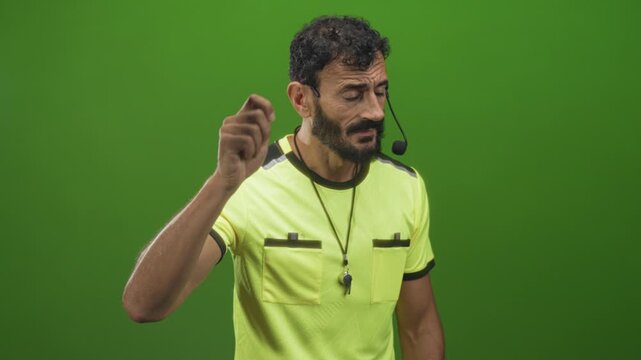 Man referee in yellow shirt pointing with hand, wearing whistle and headset in studio; authority discipline focus.