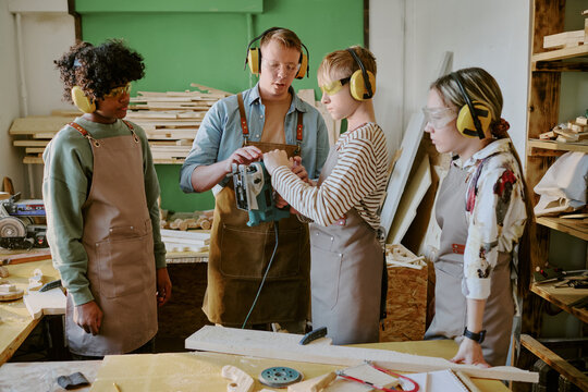 Teenagers learning woodworking, operating electric jigsaw with instructor guidance in workshop. Suitable for vocational education, skilled trades training, career program marketing
