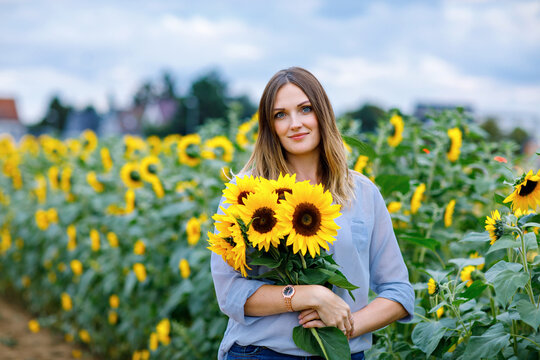 Smiling woman standing in a sunflower field holding a bouquet of bright yellow sunflowers, calm summer portrait outdoors, natural real life moment.