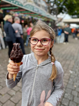 Little girl eating a big chocolate ice cream in a cone at a fair