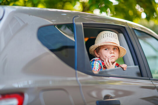 Little boy sitting in car and waving while family goes on summer road trip. Happy child enjoying travel, real life, real people.