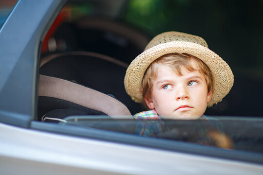 Sad little kid boy sitting in car during traffic jam on the way to summer vacation with his parents. Tired and exhausted child unhappy about the journey. Real family, real people, long car trip.