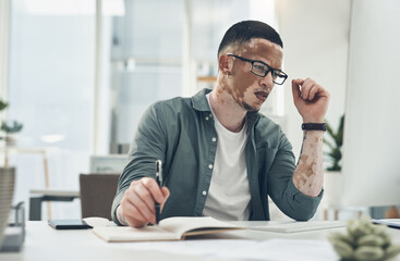 Obraz premium Man, reading and notebook in office with computer, problem solving and planning for digital marketing. Journal, desktop and person with vitiligo, glasses and thinking for online advertising project.