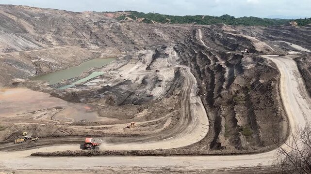 High angle wide shot of deep open-pit coal mining site with terraced landscape and heavy industrial machinery