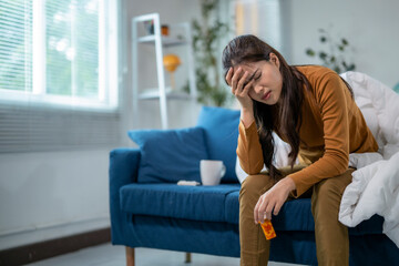 Obraz premium Sick asian woman suffering from headache holding medicine at home