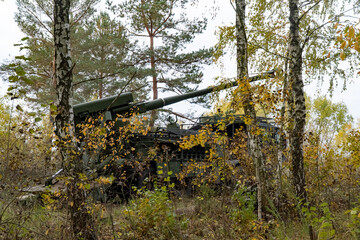 Obraz premium Camouflaged Artillery Position, self-propelled artillery mount in the forest on position. The military vehicle is camouflaged