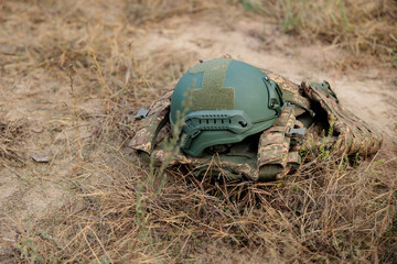 Obraz premium Helmet and bulletproof vest lesion the ground. Military equipment, military protection. Military uniform on a grass background