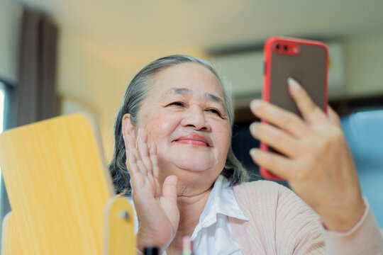 Joyful elderly Asian woman at home, enjoys and smiling while taking a selfie with her smartphone
