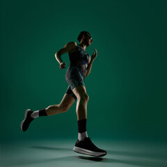Fototapeta premium Male athlete stepping forward in running low angle motion on dark green background. Concept of fitness progress visuals, training routine promotion, active lifestyle content, sports branding material.