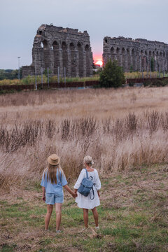 Mother and teenage daughter holding hands in Parco degli Acquedotti Rome walking toward ancient Roman aqueduct at sunset travel moment in Italy