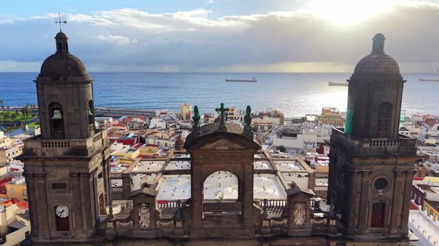 Aerial shot of Las Palmas Cathedral showcasing its towers, clock, and facade in Gran Canaria with the city and ocean behind
