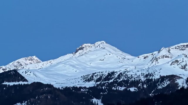 Breathtaking winter landscape featuring majestic snow covered mountain ranges and dark evergreen forests in Nauders Austria against bright blue horizon