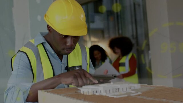 Construction site engineer tapping tablet and pointing at scale model, coordinating plans with team