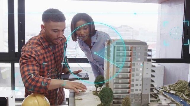Reaching duo checked-shirt blue-top tablet pointing model working with HUD yellow hardhat in office